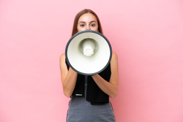 Young sport caucasian woman wearing a towel isolated on pink background shouting through a megaphone