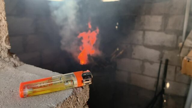 A gas lighter with a burning flame in the stove in the background