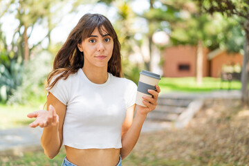 Young woman holding a take away coffee at outdoors making doubts gesture while lifting the shoulders