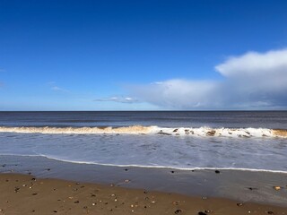 Beautiful landscape view of the vast sandy beach in Norfolk East Anglia uk with clear blue skies white cloud storm approaching calm rolling waves of sea and no people