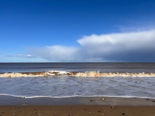 Beautiful landscape view of the vast sandy beach in Norfolk East Anglia uk with clear blue skies white cloud storm approaching calm rolling waves of sea and no people