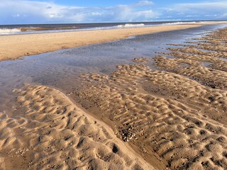 Beautiful sandy beach landscape with sand dunes and low sea tide stream water under blue sky with cloud in Spring in Norfolk East Anglis uk