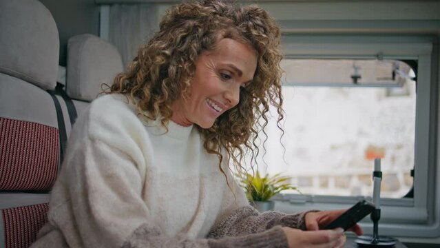 Cheerful lady watching social media at cellphone in camper van close up.