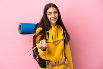Young mountaineer girl with a big backpack isolated on pink background inviting to come with hand....