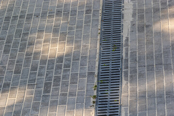 A lattice of a drainage paving system on a footpath made of square stone tiles, close up of a rainwater drainage system