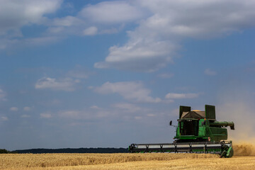 Photo of combine harvester that is harvesting wheat with dust straw in the air