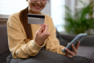 Happy young woman holding credit card and smartphone paying online or using banking service
