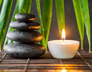 Still life spa setting featuring stacked stones, a burning candle, and bamboo leaves