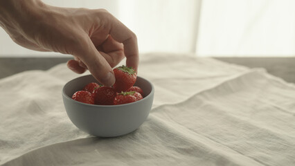 man take fresh strawberries from blue bowl on linen napkin