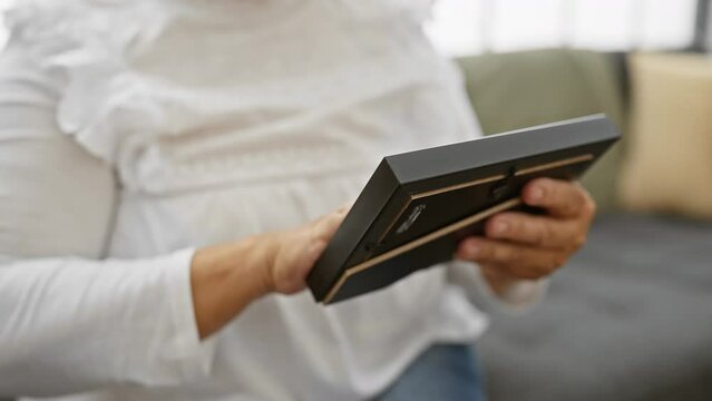 Mature woman holding photo album at home looking reminiscent