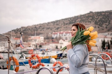 Woman holds yellow tulips in harbor with boats docked in the background., overcast day, yellow...