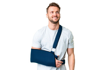 Young caucasian man with broken arm and wearing a sling over isolated chroma key background thinking an idea while looking up - obrazy, fototapety, plakaty