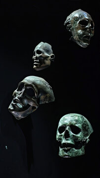 Three bronze mask heads, one skull and two ancient Greek masks, floating in the air, with a black background Green enamel sits