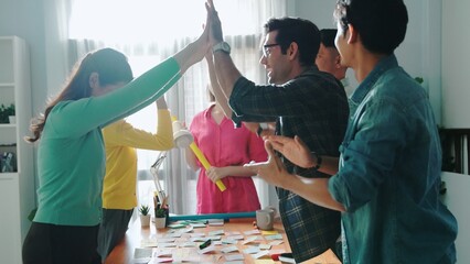 Professional business team give high five to celebrate project while standing at table with sticky...