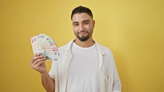 Cheerful young arab man with uae banknotes flashing an excellent ok sign, radiating positivity over yellow isolated backdrop