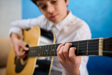 Details on the hands of boy guitarist musician in white casual shirt, plucking strings while...