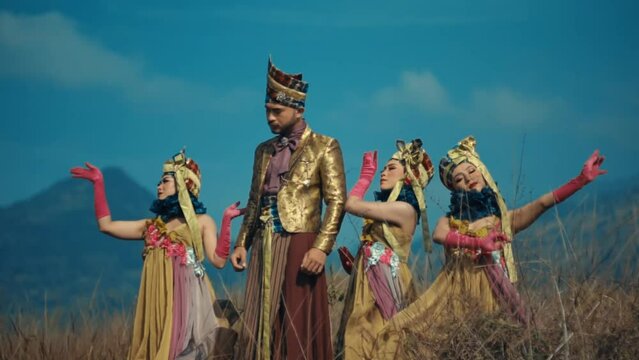 Traditional Indonesian dancers in elaborate costumes performing outdoors with a scenic mountain backdrop.