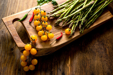 asparagus and a branch with yellow cherry tomatoes on a wooden board.
- 771395129