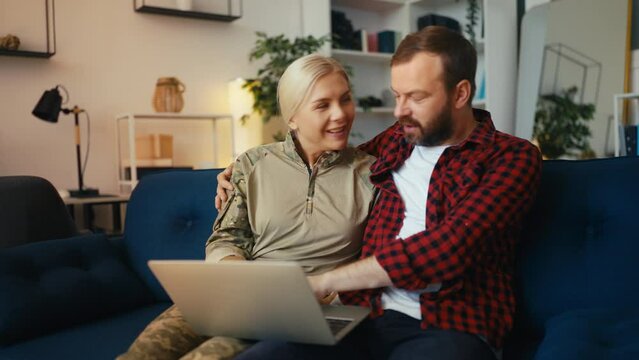 Happy man and military wife shopping online using laptop, having fun together
