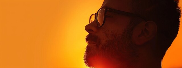 An introspective man wearing glasses against a sunset-orange backdrop symbolizing deep thoughtfulness