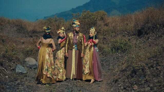 Three people in traditional Balinese attire standing on rocky terrain with mountains