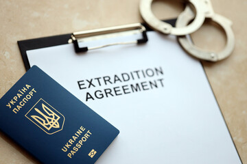 Passport of Ukraine and Extradition Agreement with handcuffs on table close up