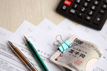 Japanese tax forms lies on table with calculator, pen and japanese yen money bills roll close up