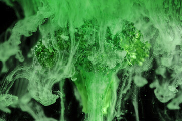 Fresh broccoli with a cloud of green color paint on black background. Artistic nutrition concept....