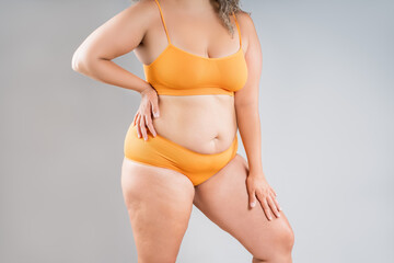 Fat woman in orange underwear on gray background, obesity and cellulite, overweight female body,...