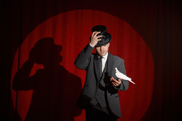 Portrait of magician with pigeon standing over red drapery in spotlight