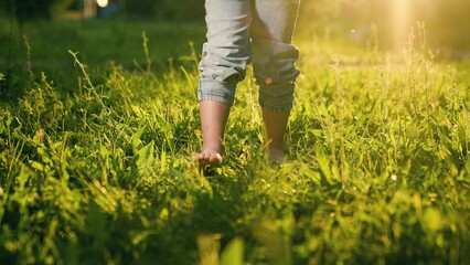 Children feet walk on green grass in summer, slow motion. Little bare legged kid girl, Healthy baby...