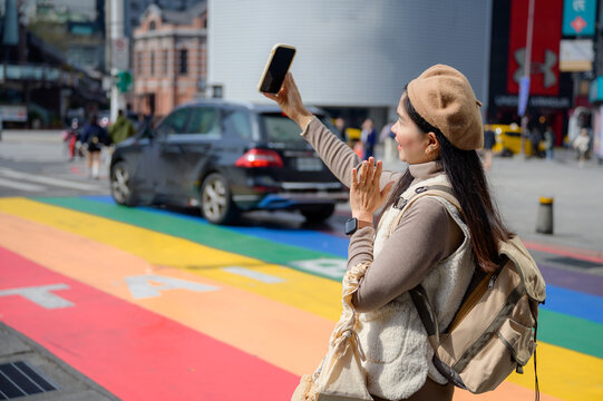 Asian female tourist uses mobile phone to take a selfie of herself on Rainbow Street at Ximending landmark and popular tourist attraction in Taipei, Taiwan.