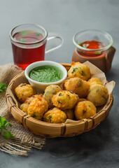 Crispy moong dal pakoras served in a bamboo bowl with green chutney and tea on a grey background