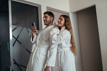 Pareja feliz andando en albornoz por hotel tomando fotos