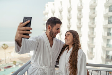 Pareja feliz andando en albornoz por hotel tomando fotos