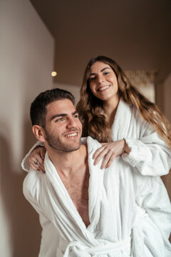 Pareja feliz andando en albornoz por hotel tomando fotos