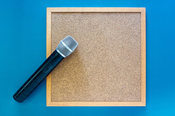 Blank cork board in wooden frame on blue background with a wireless microphone in top view