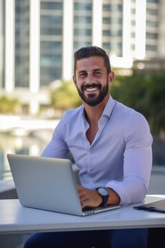 A young businessman man with a smile on his face sits outdoors with a laptop against the background of skyscrapers. Generative AI.