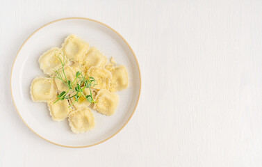 Top view of homemade traditional italian ravioli pasta made with   dough stuffed with ricotta cheese decorated with pea microgreens and parmesan served on plate on white wooden table with copy space