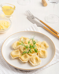 Homemade italian ravioli pasta of square shape stuffed with ricotta cheese decorated with pea microgreen and grated parmesan served on plate on white wooden table with glass of wine and tableware 