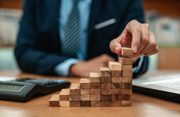 achievement, ambition, conceptual, leadership, management, strategy, growth, stability, progress, plan. A man is building a wooden blocks. The blocks are stacked on top of each other. - obrazy, fototapety, plakaty