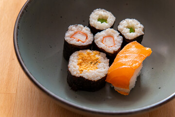 bowl of assorted sushi sits on a wooden table