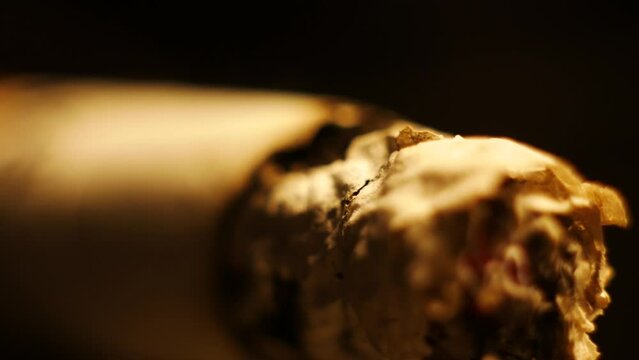 Video Macro shooting of a cigarette smoldering while smoking. Ashes can be seen falling and a cigarette burns.