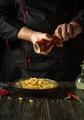The chef adds hot peppers to a plate of pasta. Working environment on the kitchen table in the cook room. Delicious pasta with vegetables for lunch