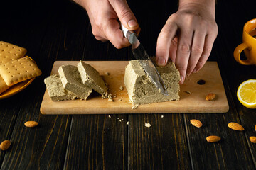 Cutting halva with a knife in the hands of a chef on a cutting board in a restaurant kitchen. Low...