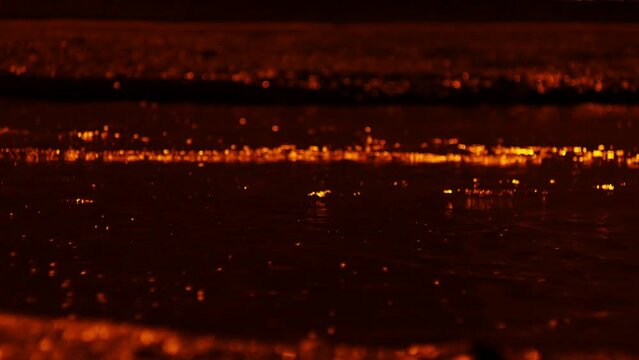A puddle on a city street with dirty water during a rainstorm at night. Close-up shot of a car driving through a puddle.