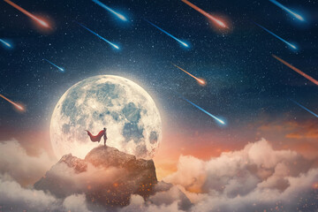 Conceptual night scene with a superhero with cape standing brave on a mountain peak searching determined at horizon with hand up to forehead. Powerful hero overcoming obstacles and reaching success - obrazy, fototapety, plakaty