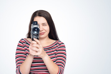 A happy young girl shoots a movie with an old film camera, front view, isolated on a light blue background