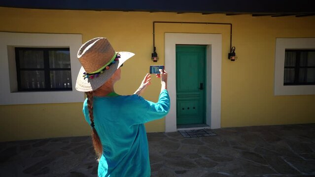 Mature woman tourist wearing straw hat and ethnic, traditional clothes taking photos with phone in front of old building in mining town of El Triunfo, Mexico.