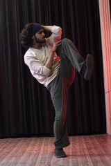 An Indian Modern Dancer Boy Wearing over sized full sleeves T-Shirt and loose lower pants, dancing and posing in front of black curtain, modern